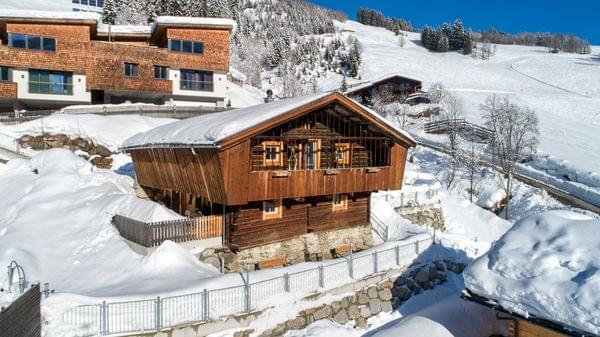 Alpines Holzchalet in verschneiter Berglandschaft nahe Skipisten und Nadelwald