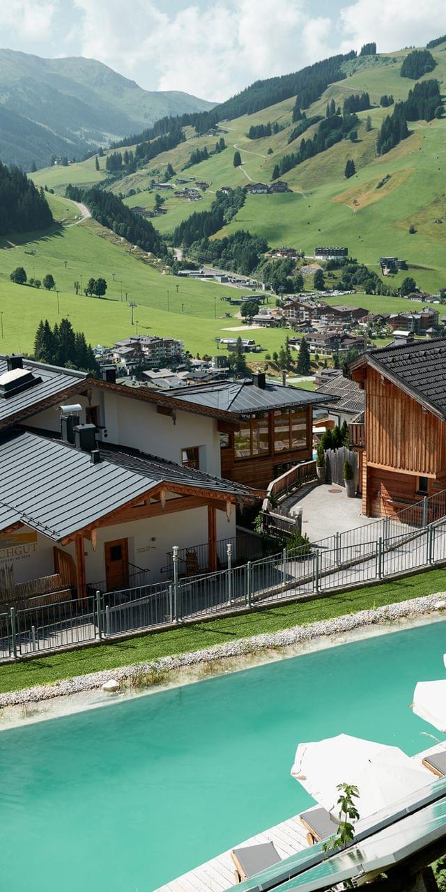 Luxury alpine resort with pool and wooden chalets overlooking mountain valley in summer