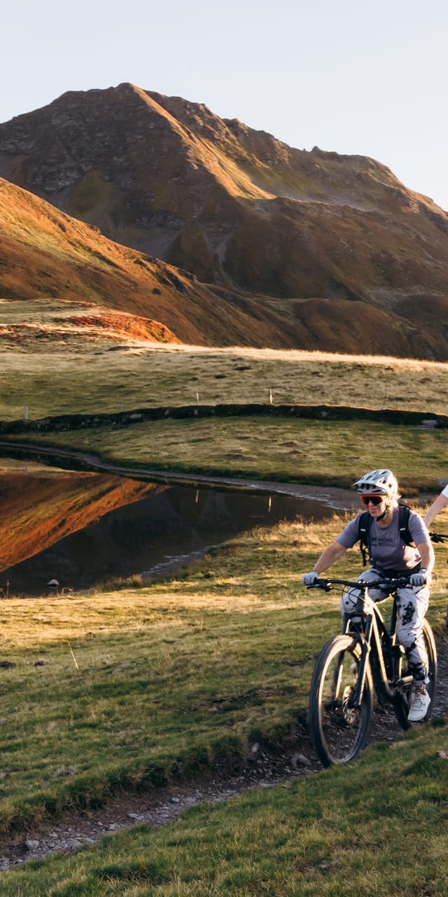 Two mountain bikers riding along a trail on the mountain, with an autumn landscape.