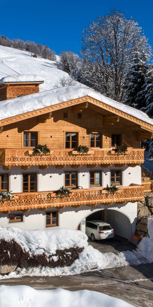 Traditionelles Alpenchalet im verschneiten Bergdorf unter klarem blauen Himmel