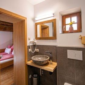 Gemütliches Bad mit Steinwaschbecken, Holzelementen und Blick in ein rustikales Schlafzimmer