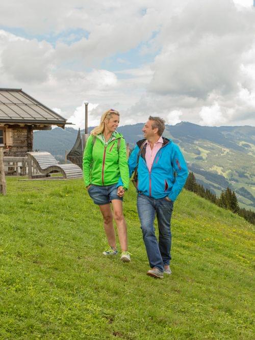 Paar wandert in den österreichischen Alpen nahe einer Berghütte mit Panoramablick ins Tal