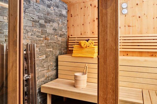 Moderner Holzsauna-Innenraum mit gestapelten gelben Handtüchern und Saunakübel
