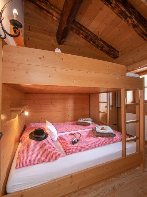 Gemütliches Schlafzimmer in Holzhütte mit Etagenbett, rot karierten Bettdecken und rustikaler Alpendekoration