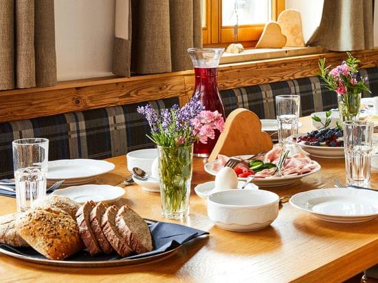 Rustic breakfast table with bread, cold cuts, berries, juice, coffee and flowers by a sunny window
