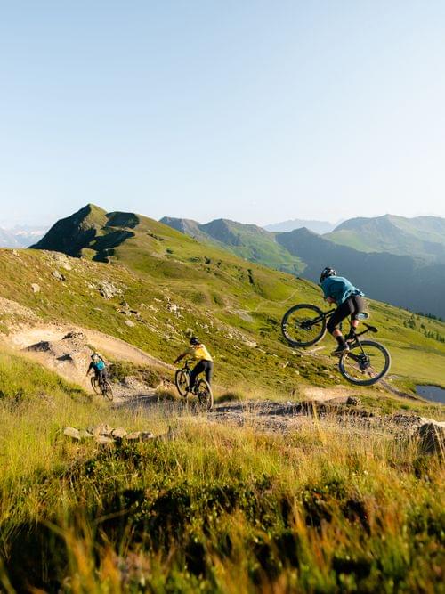 Mountainbiker fahren und springen auf einem Trail durch grüne Alpenhügel im Sommer