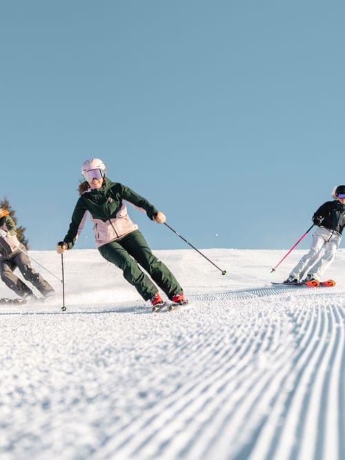 Drei Skifahrer carven auf frisch präparierter Piste unter klarem Himmel