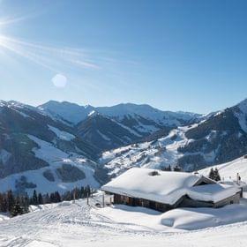 Bachalm Außenansicht im Winter, Berge in Schnee gehüllt und Sonnenschein 