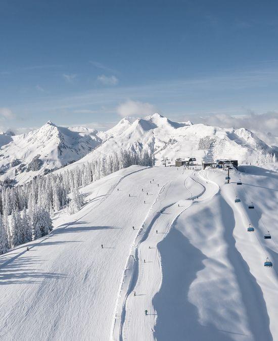 Skigebiet mit verschneiten Pisten, Sesselliften und Alpenpanorama unter blauem Himmel