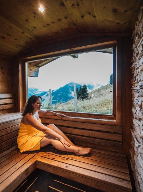 Frau in Sauna die durch Panorama Fenster nach draußen blickt 