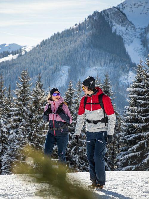Zwei Wanderer in bunter Winterkleidung spazieren durch verschneite Alpenlandschaft