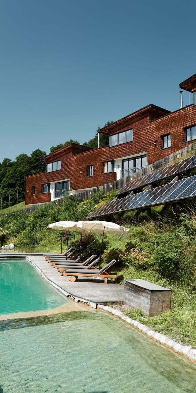 Öko-Hotel mit Holzfassade, Solarpaneelen und Sonnenliegen am Naturpool
