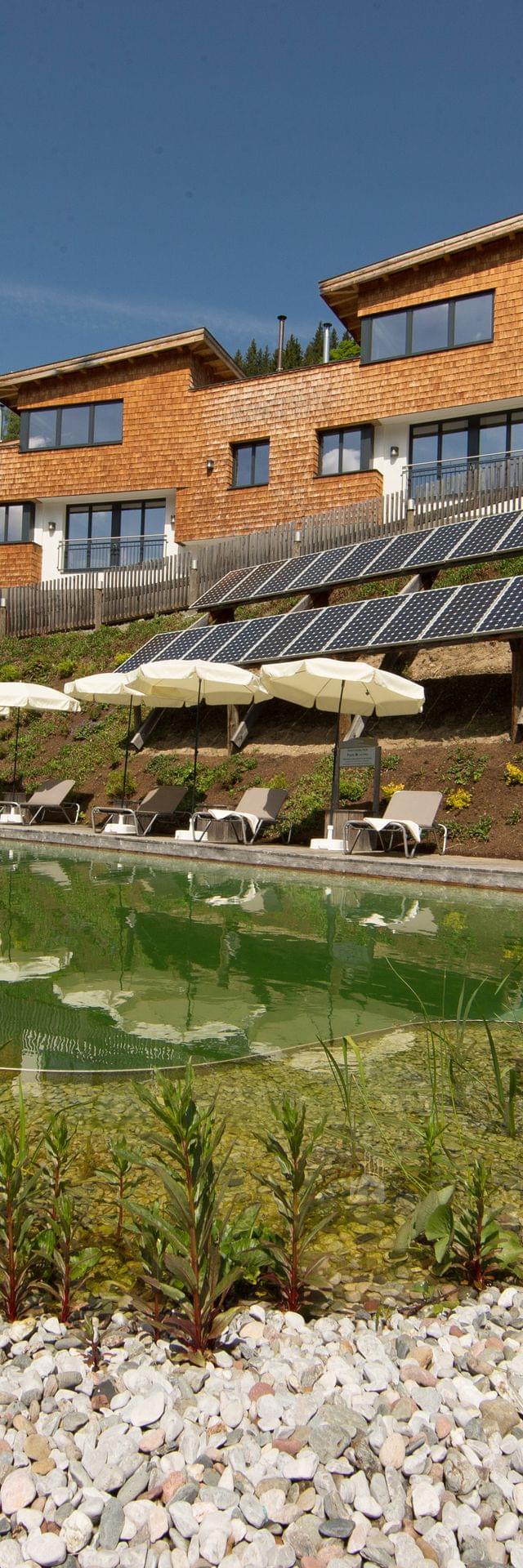A view of the natural swimming pond and the Bachgut chalets clad in wood.