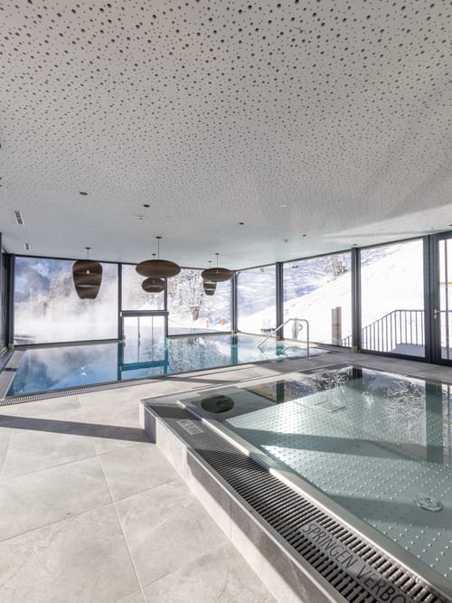 Bachgut Badehaus mit Kinder-Innenbecken und Schwimmbecken das nach draußen in den Invinity-Pool führt. Tief-Winterlich verschneite Landschaft im Hintergrund 