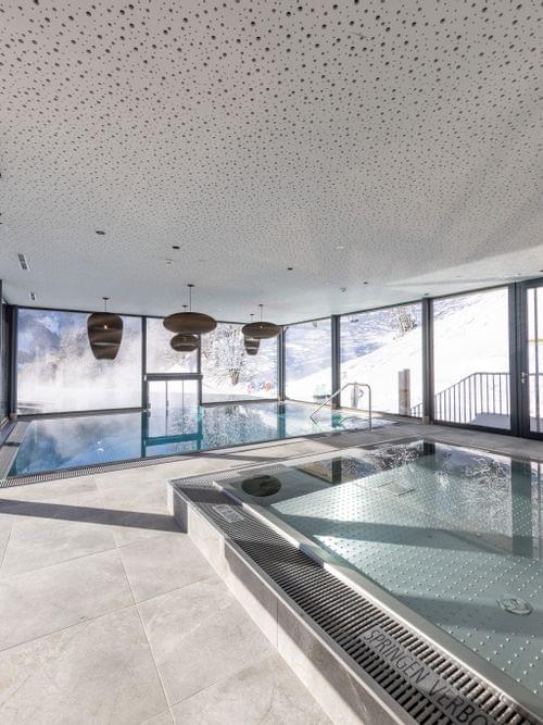 Bachgut Badehaus mit Kinder-Innenbecken und Schwimmbecken das nach draußen in den Invinity-Pool führt. Tief-Winterlich verschneite Landschaft im Hintergrund 