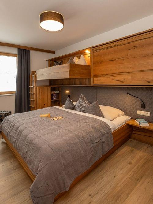 Modern alpine hotel room with wooden furniture, double bed and overhead bunk bed