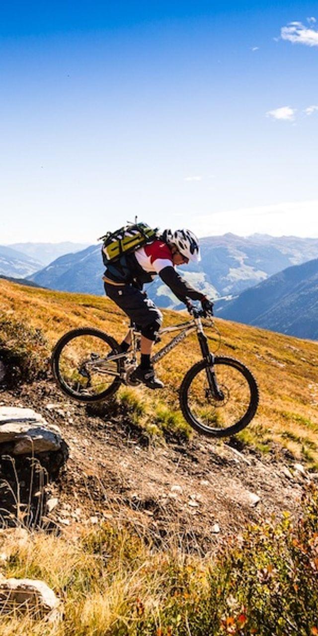 Zwei Mountainbiker fahren bergab auf einem alpinen Trail unter blauem Himmel
