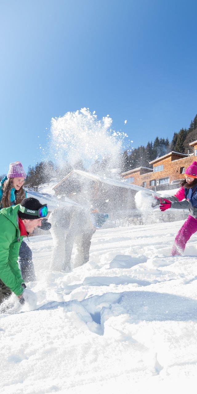 Kinder spielen im Schnee während Winterurlaub bei Alpenchalets an sonnigem Tag