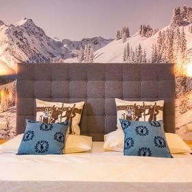 Cozy double hotel bed with alpine-themed pillows and snowy mountain wall mural