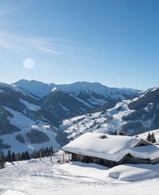 Bachalm Außenansicht im Winter, Berge in Schnee gehüllt und Sonnenschein 