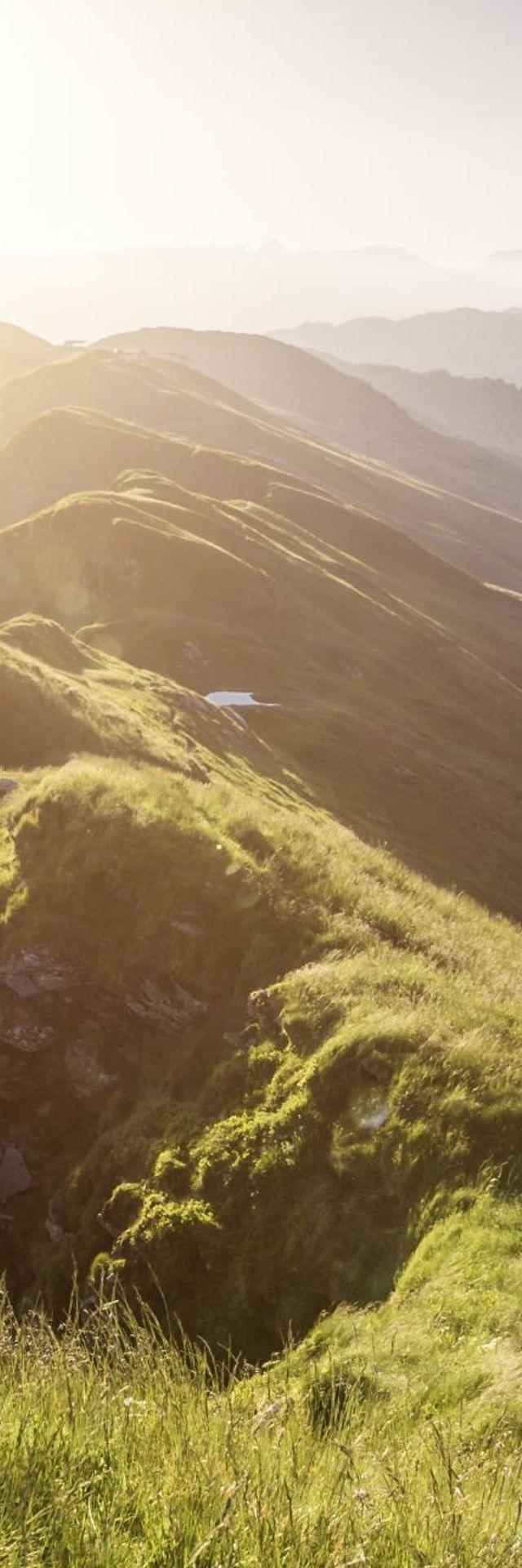 Wanderer auf einem Berggrat bei Sonnenaufgang mit alpiner Landschaft im Hintergrund