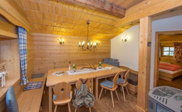 Gemütliches alpines Esszimmer aus Holz mit Kronleuchter, rustikalen Möbeln und angrenzendem Schlafzimmer