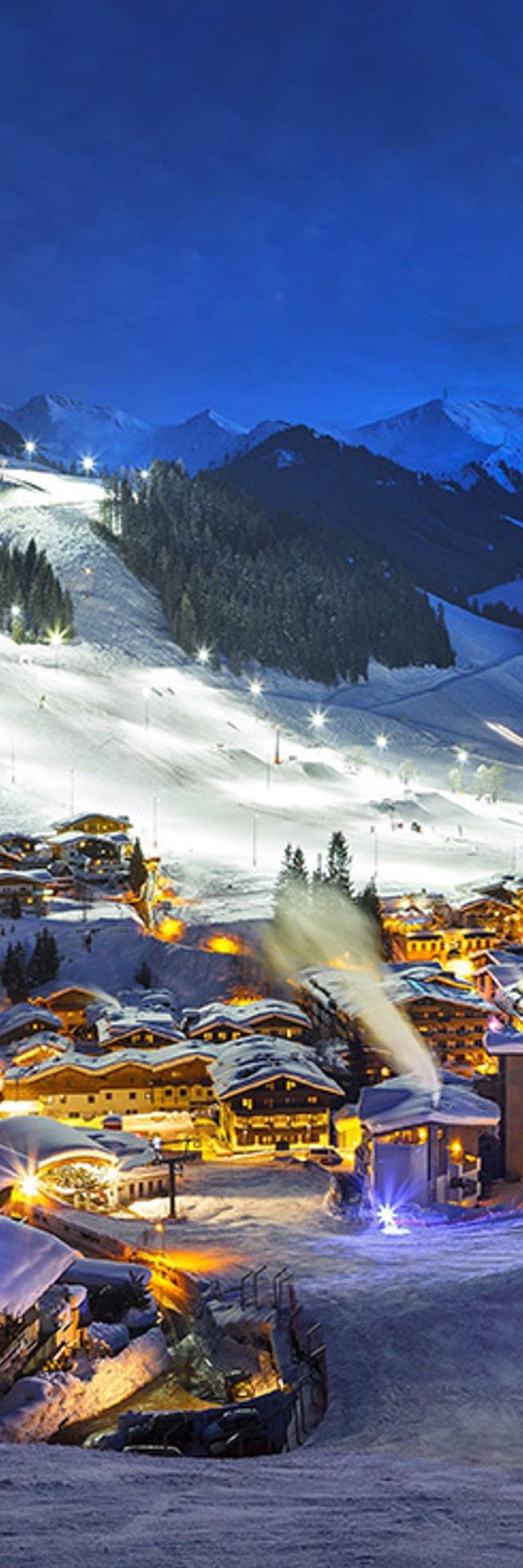 Alpine ski resort village illuminated at night with snowy slopes and mountain landscape