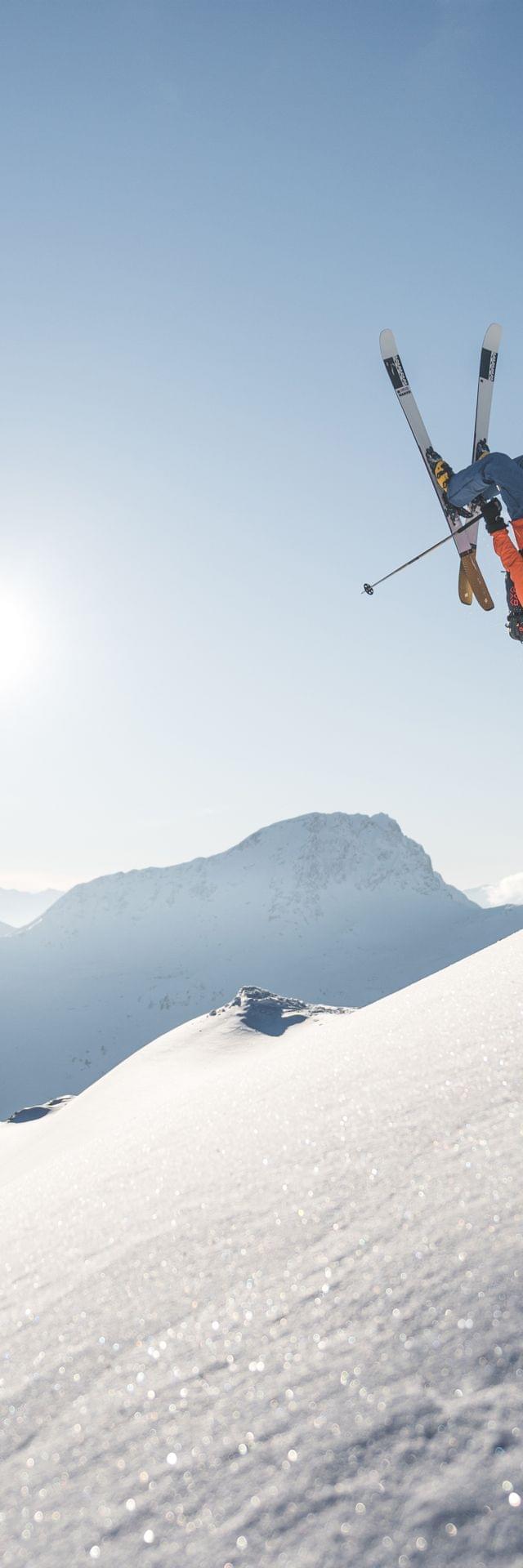Freestyle skier performing backflip over snowy mountain slope under clear blue sky