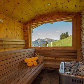 Holzsauna mit Blick auf Berge durch großes Fenster und gefalteten Handtüchern auf der Bank