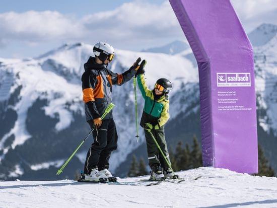 Adult and child skiers high-five on snowy slope at Saalbach ski resort in the Alps