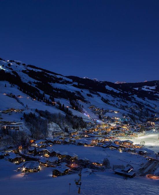 Snow-covered alpine village with ski slopes illuminated at night in winter landscape