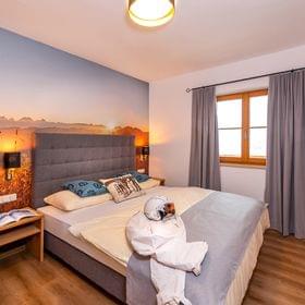 Gemütliches Hotelzimmer mit Berg-Sonnenuntergang-Wandbild und Skiausrüstung auf dem Bett