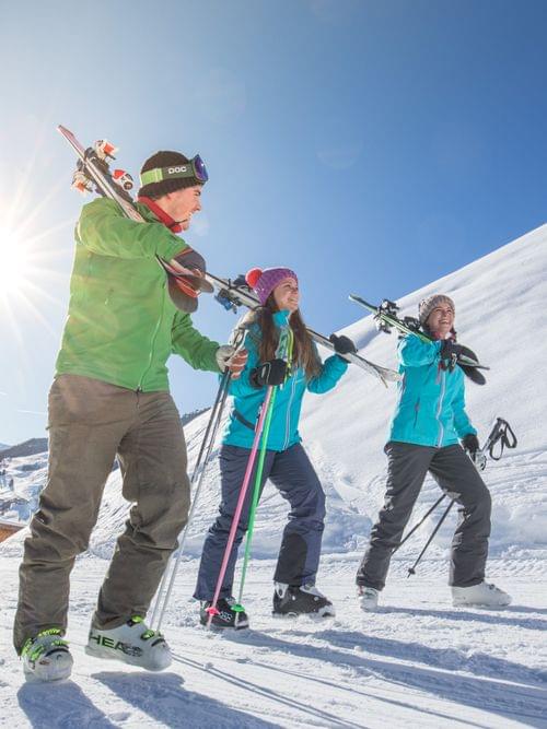 Gruppe von Skifahrern geht bei Sonnenschein mit Skiern auf den Schultern durch verschneite Alpenlandschaft
