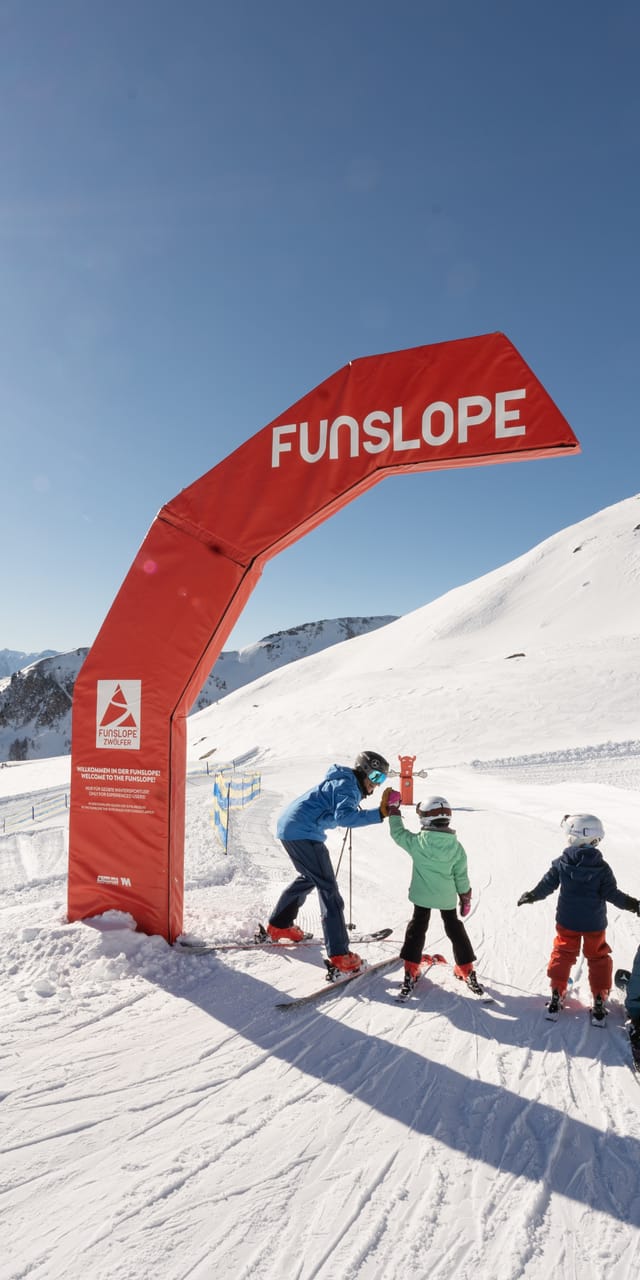 A family with two children skiing, standing by an arch marking the Snow Trail.