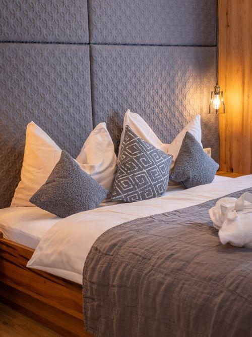 Gemütliches Hotelbett mit grauen Kissen, gepolstertem Kopfteil und warmer Beleuchtung
