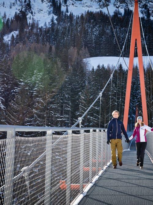 Couple walking on a suspension bridge in snowy alpine forest