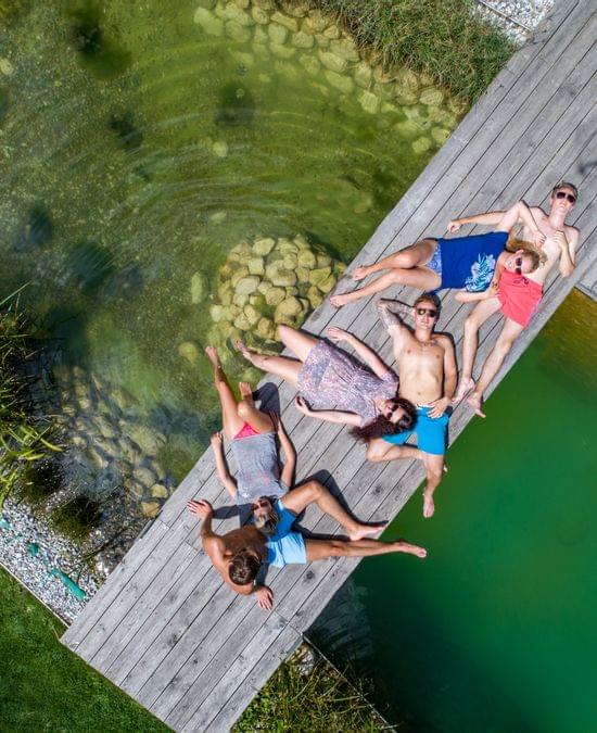 Freundesgruppe entspannt auf einem Holzsteg an einem Naturbadeteich