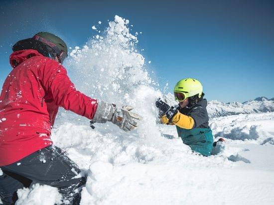 Two people playing in fresh mountain snow under blue sky in winter gear