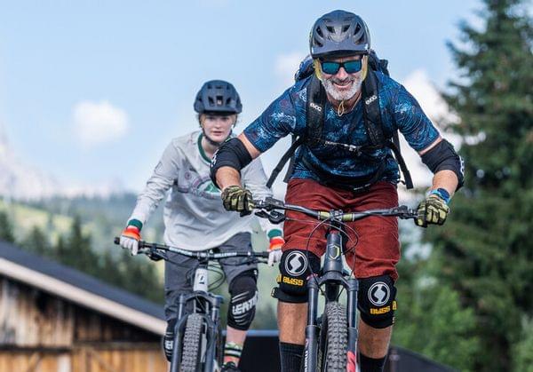 Zwei Mountainbiker fahren einen Trail in alpiner Landschaft hinunter