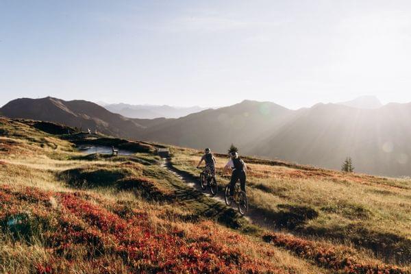 An atmospheric view of the autumn mountain landscape, with two mountain bikers riding down a trail.