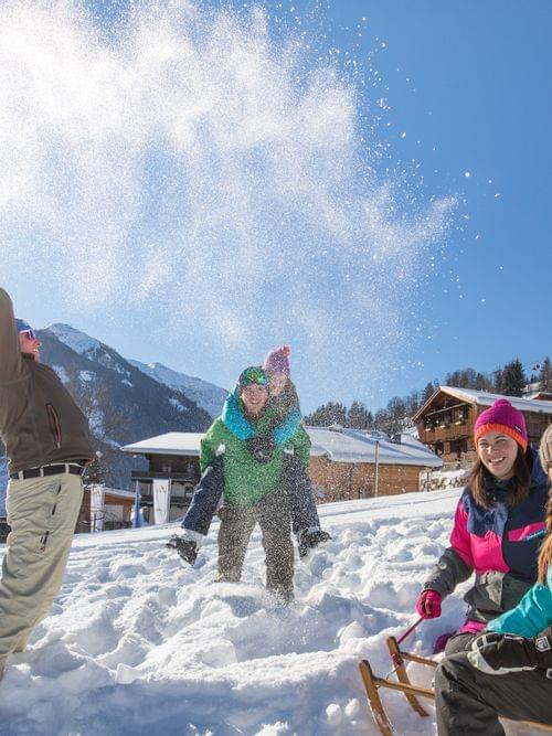 Friends playing in the snow on a sunny day near alpine ski resort chalets
