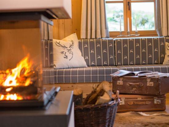 Gemütliches Alpen-Wohnzimmer mit Kamin, rustikalem Sofa, Feuerholzkorb und Vintage-Koffern
