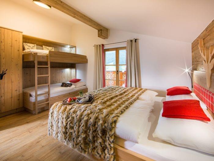 Gemütliches Alpenhotelzimmer mit Doppelbett, Etagenbetten, Felldecke und Holzelementen