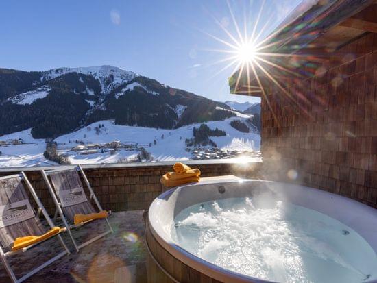 Sprudelnde Whirlwanne auf der Terrasse mit Liegestühlen und Ausblick auf die Sonnige und verschneite Bergwelt 