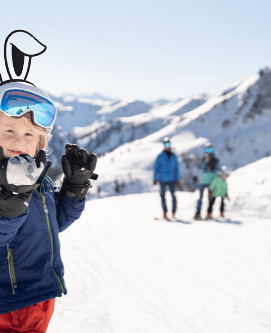 A child with their family in the snow, holding a snowball and wearing a ski helmet with bunny ears like an Easter bunny.