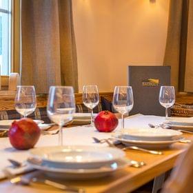 Gemütlich gedeckter Restauranttisch mit Tellern, Weingläsern, Granatäpfeln und Bachgut-Menü