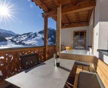 Ausblick von der Terrasse der Stammhaus Suiten auf die Berge von Saalbach Hinterglemm im Winter, auf der Terrasse ist ein Whirlpool und eine gemütliche Stizgelegenheit zu sehen. 
