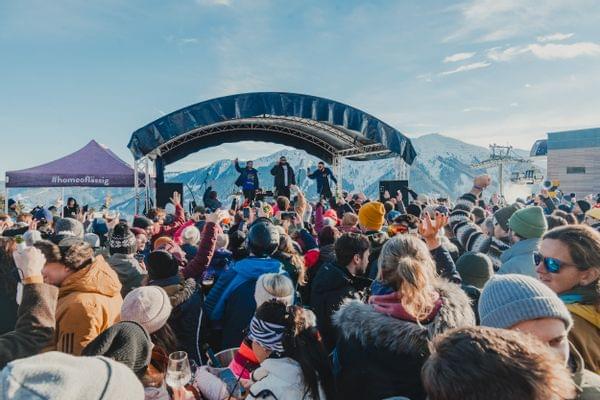 Eine Festivalbühne mit vielen Leuten davor, im Hintergrund die Berge und Schnee 