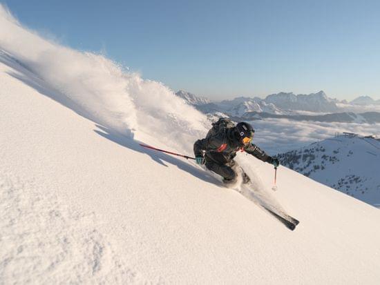 Freeride-Skifahrer carvt durch Pulverschnee auf steilem Alpengelände bei Sonnenaufgang