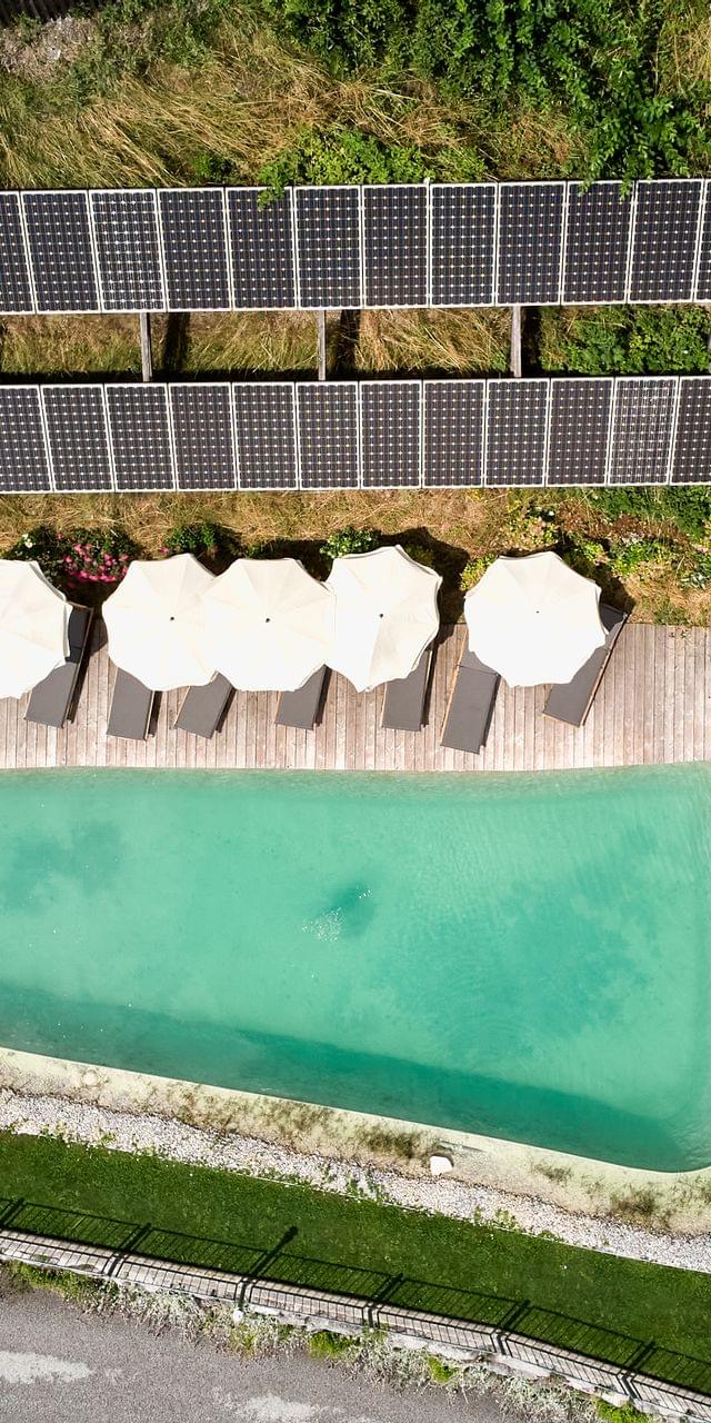 Vogelperspektive von Bachgut Naturbadeteich, Rundherum mit Liegen und Sonnenschirmen und ein Teil der Photovoltaik Anlage 